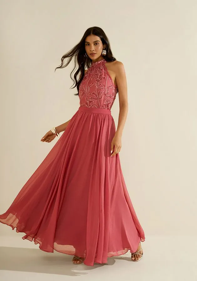 Modelo em movimento com vestido longo rosa de corpo bordado e saia ampla